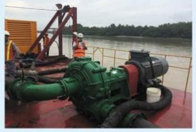 Green dredge pump and pipework on a river barge.